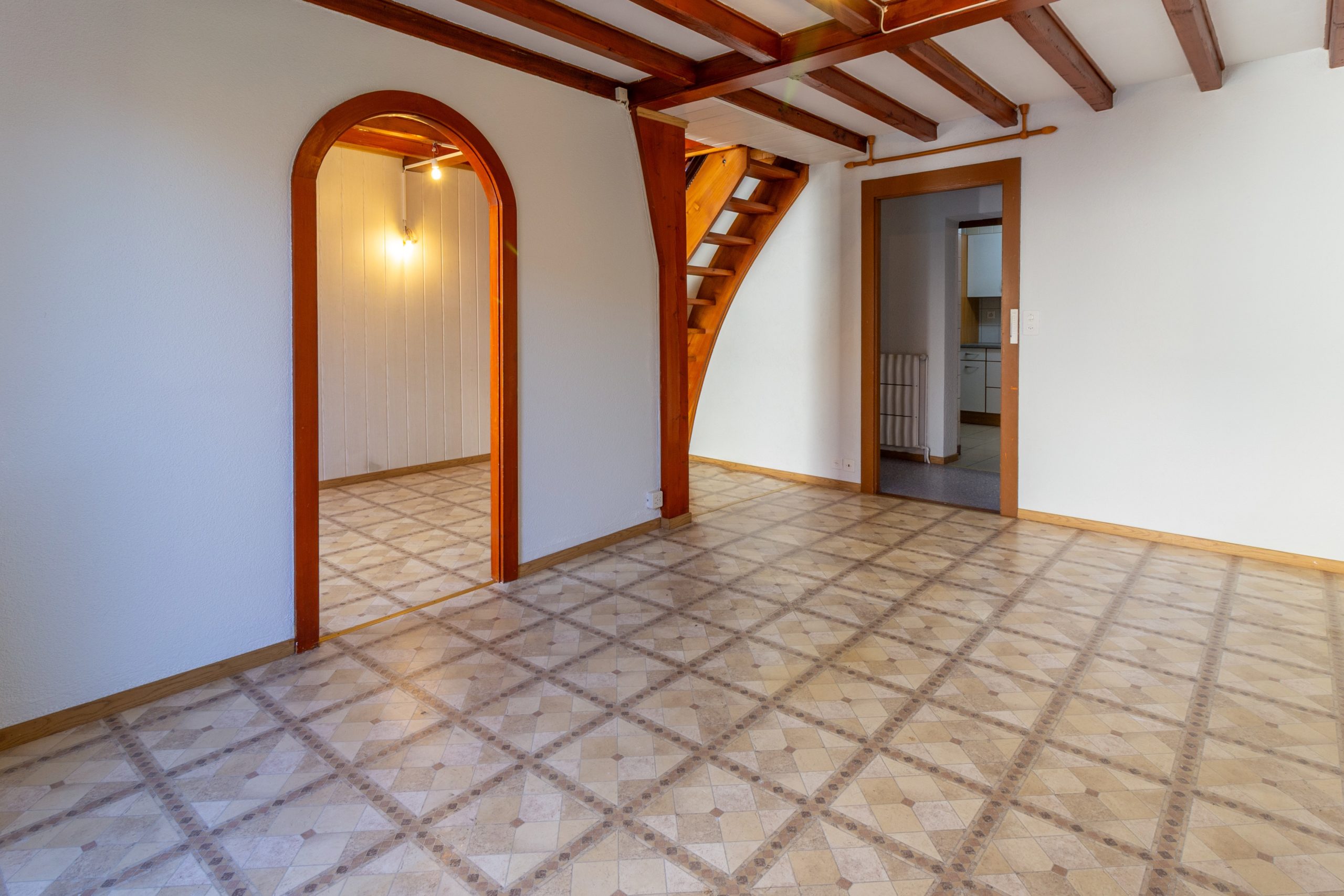 Leerer Wohnraum mit Holztreppe und Fliesenboden