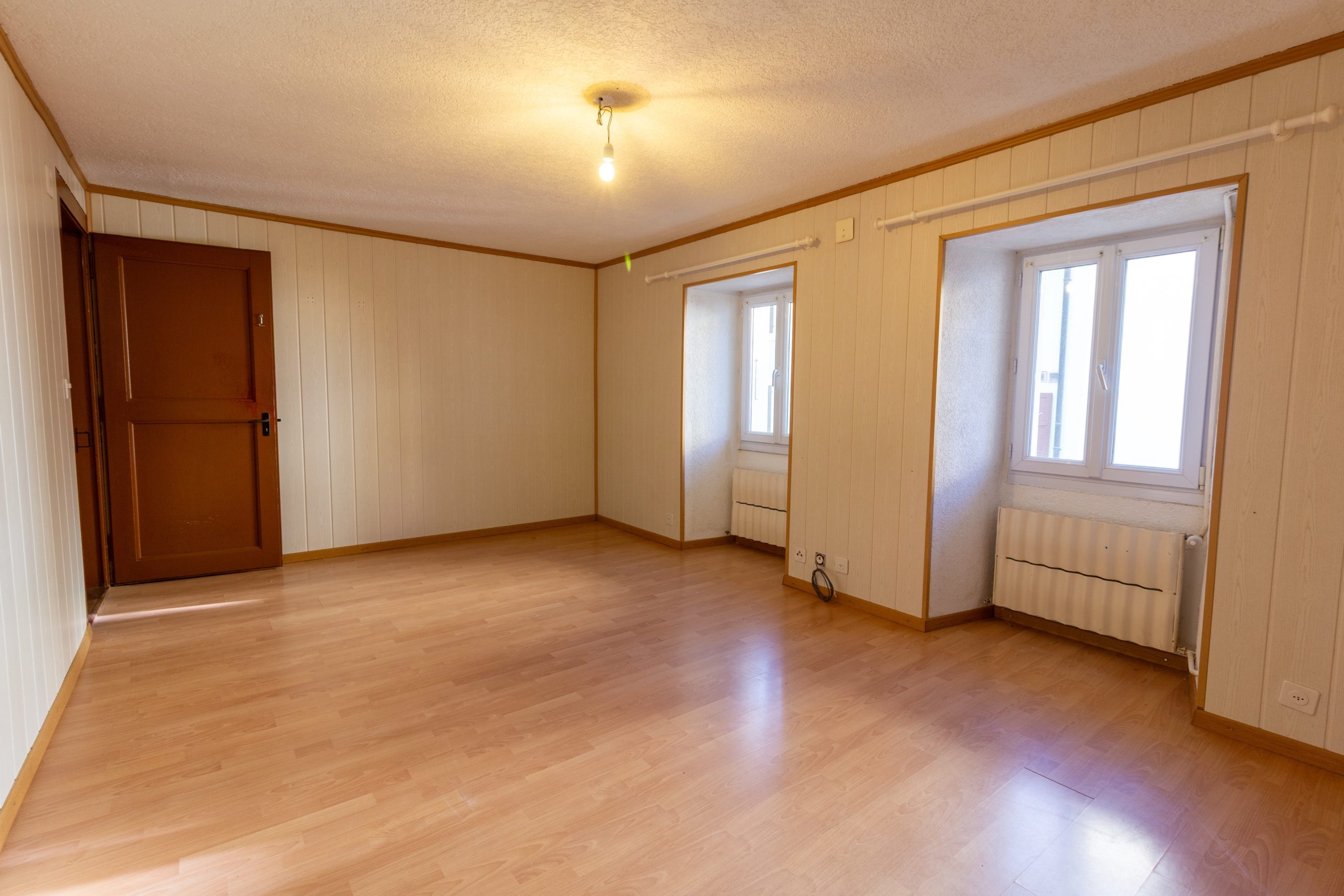 Leeres Zimmer mit Holzoptik und zwei Fenstern
