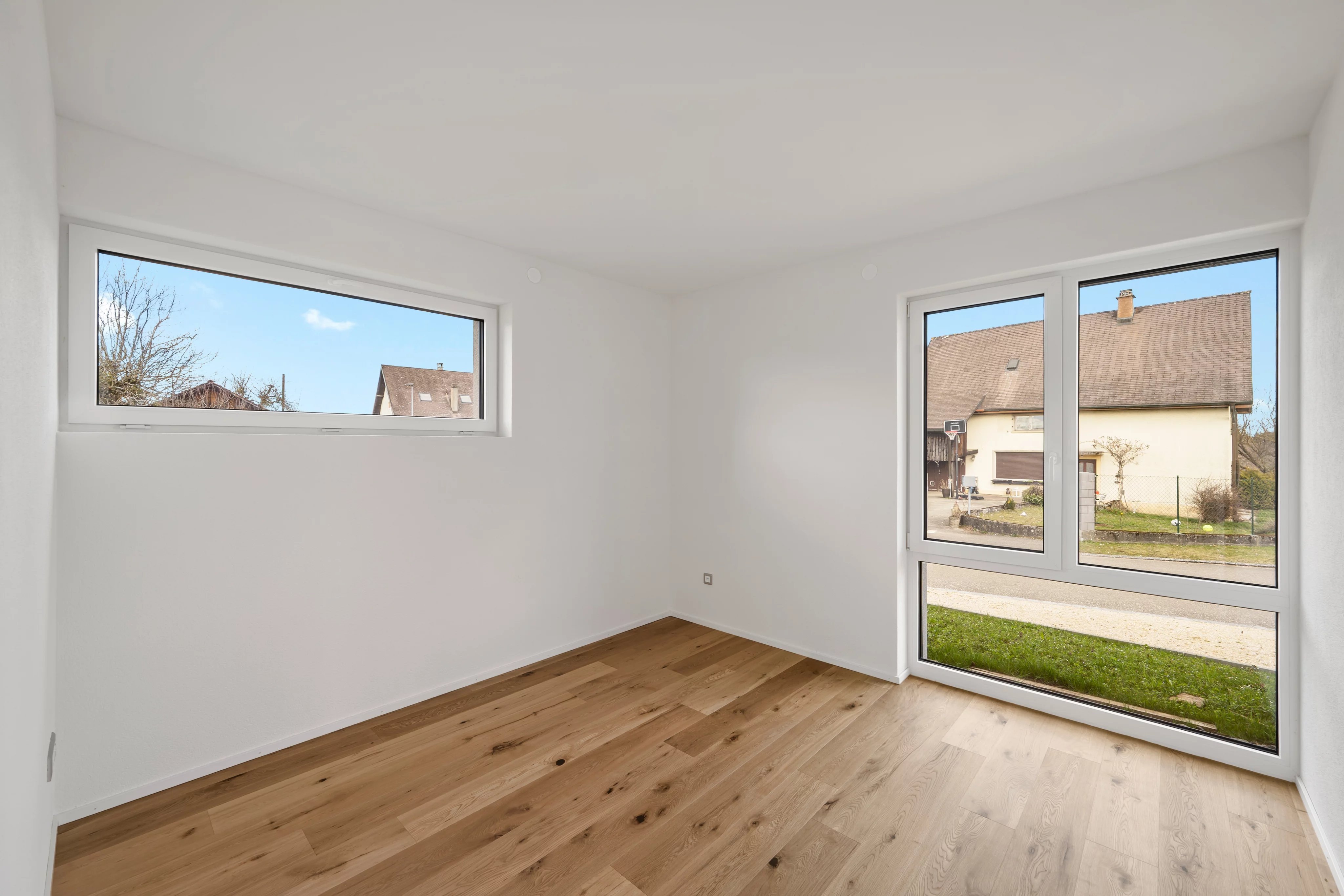 Heller, leerer Raum mit großen Fenstern und Holzboden