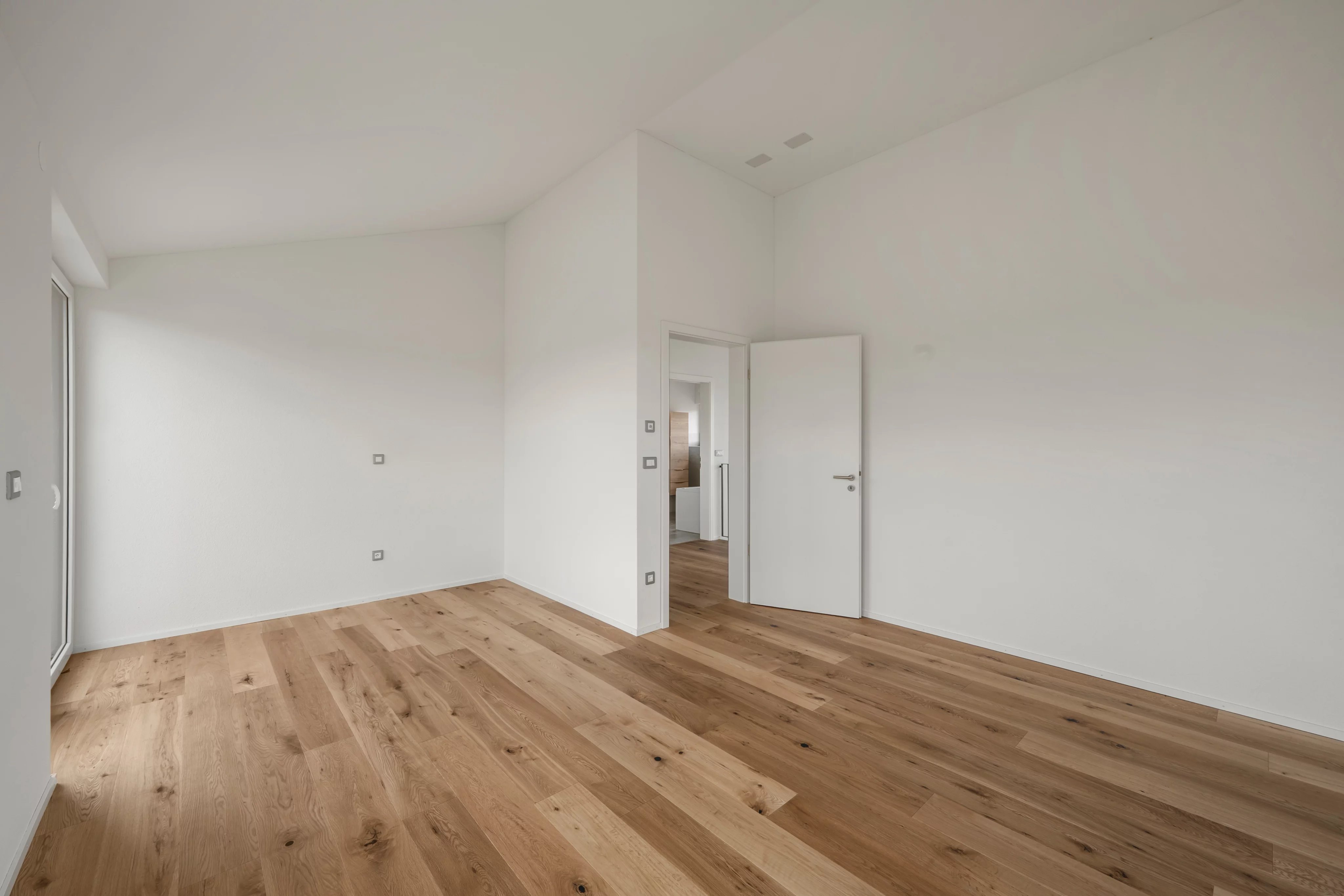 Heller leerer Raum mit Holzboden und weißen Wänden