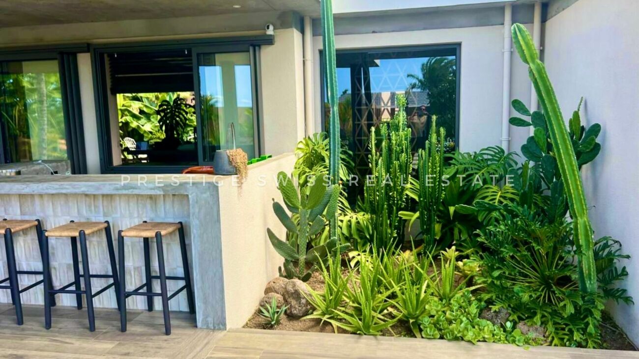 Überdachte Terrasse mit Barhockern und üppiger Bepflanzung