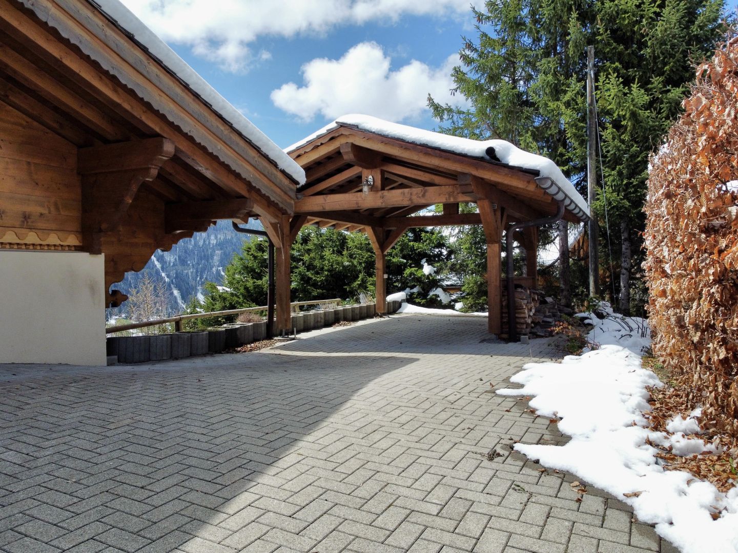 Schneebedeckter Holzcarport mit gepflasterter Zufahrt
