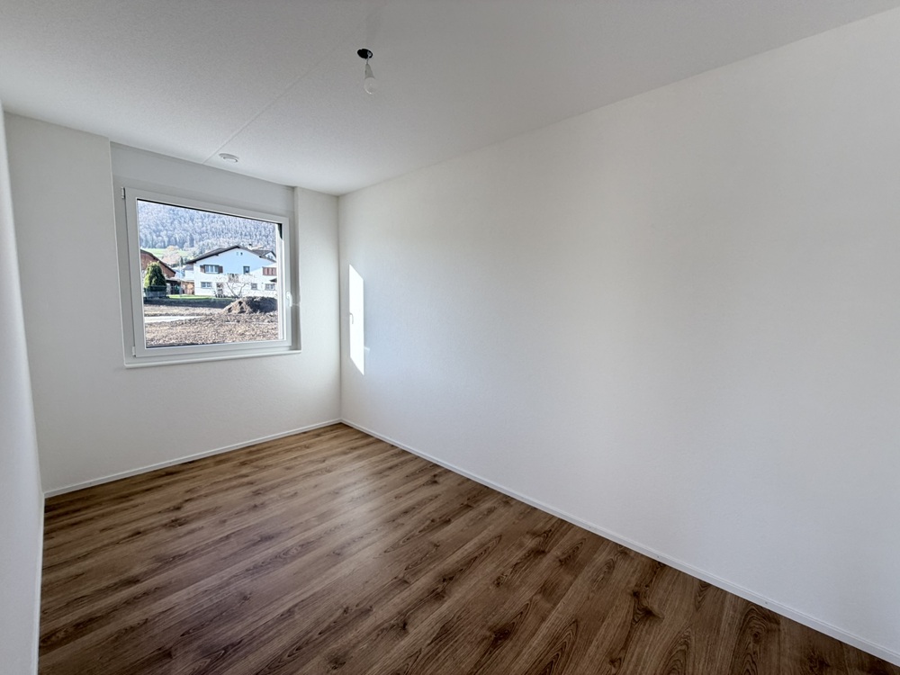 Helles, leeres Zimmer mit Holzoptik-Boden und Fensterblick
