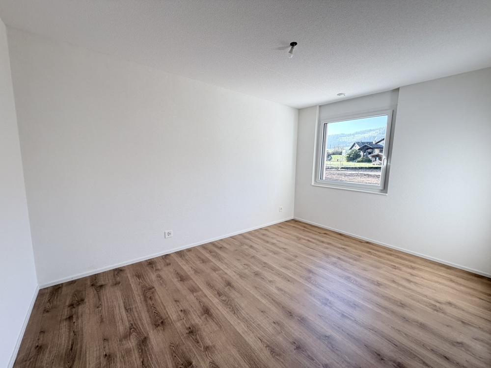 Leerer heller Raum mit Holzoptikboden und Fensterblick