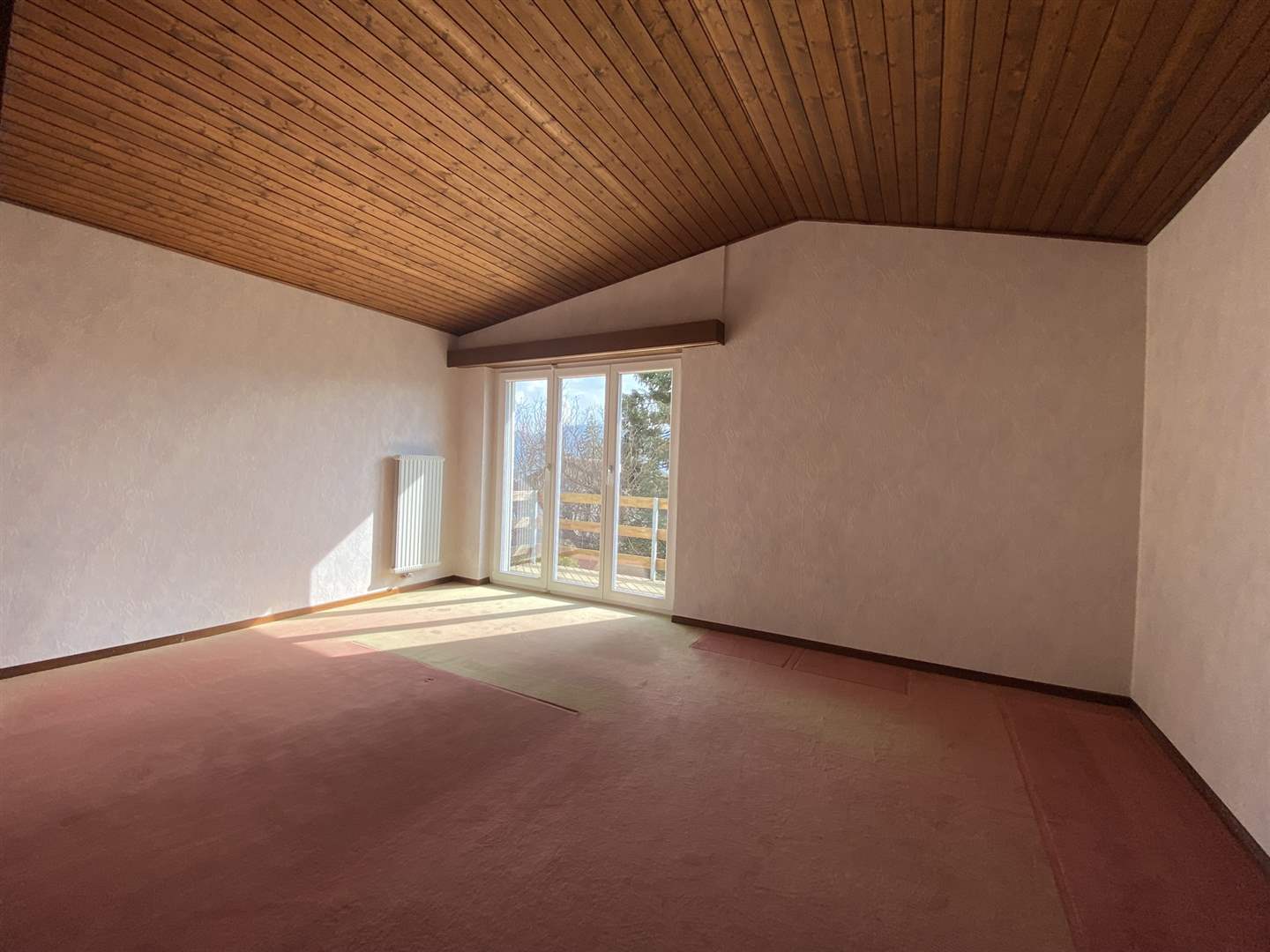 Heller leerer Raum mit Holzdecke und Balkonfenster