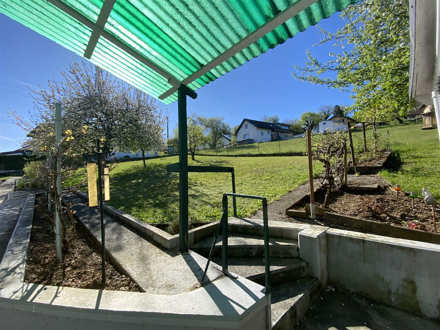 Garten mit Betonwegen und grünem Vordach