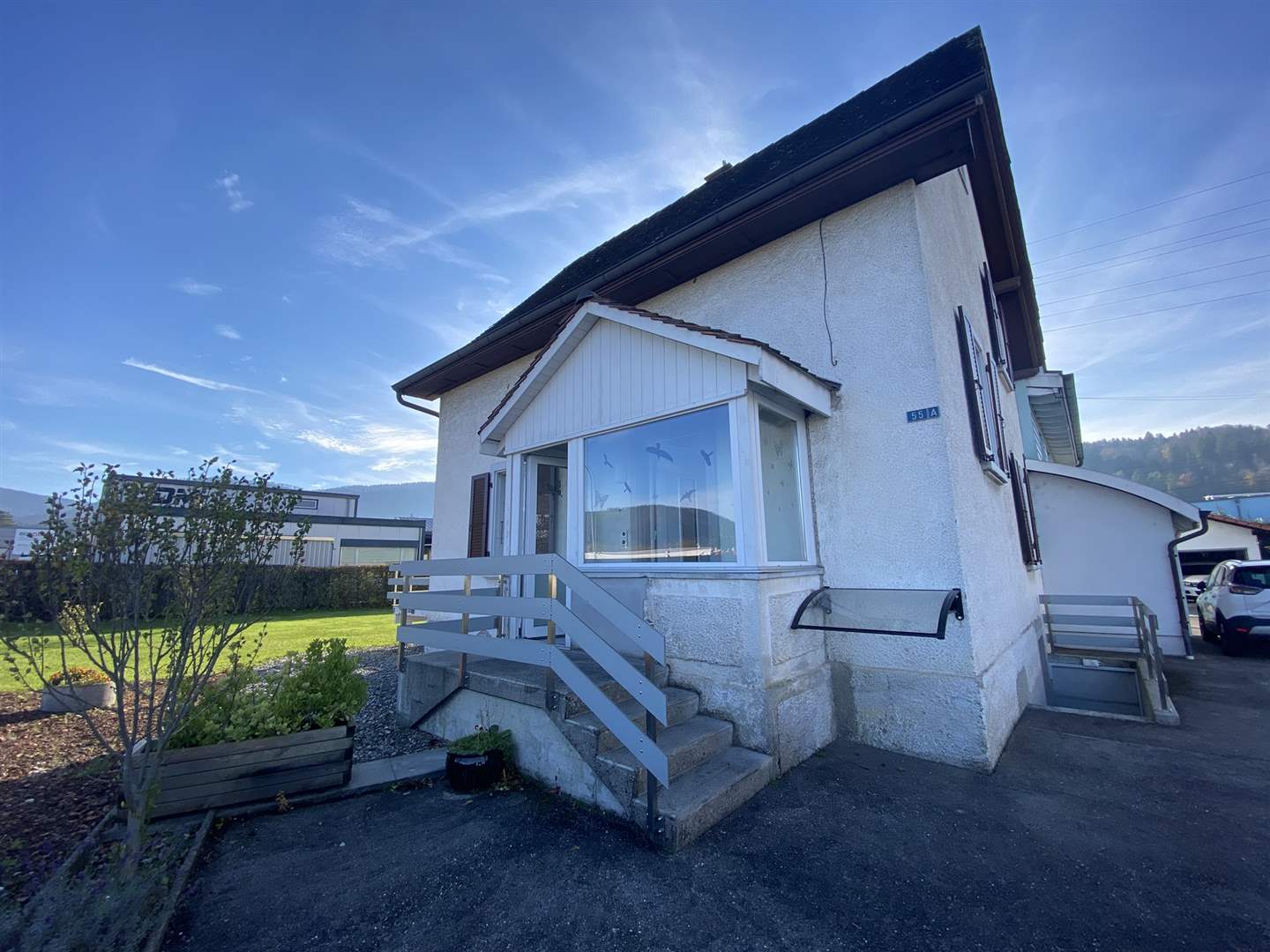 Ein kleines Einfamilienhaus mit weiß verputzter Fassade, dunklem Dach und einem verglasten Vorbau am Eingang.