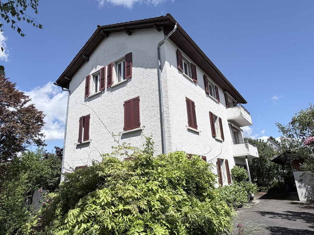 Wohnhaus mit weißer Fassade und roten Fensterläden