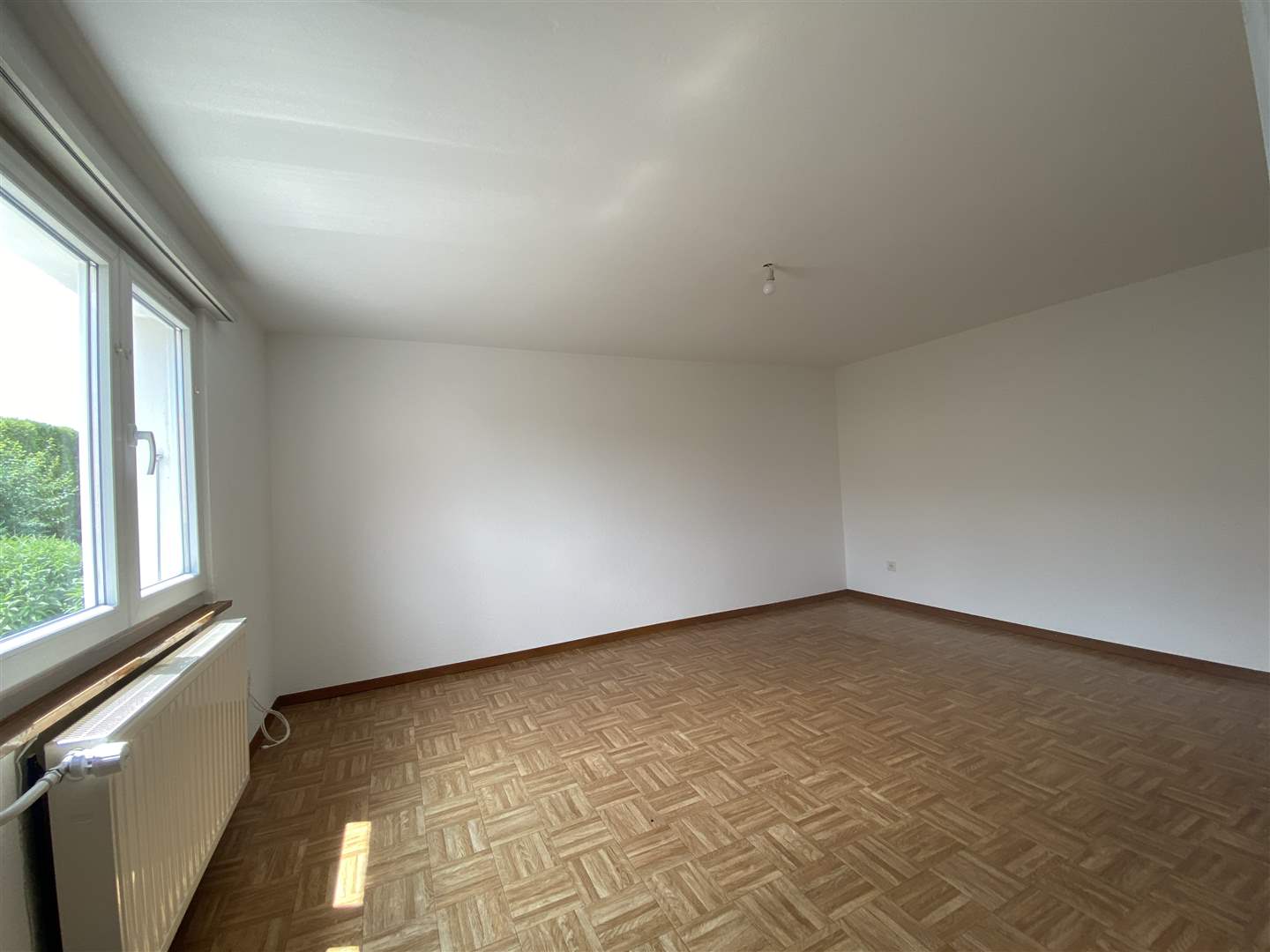 Leerer heller Raum mit Fenster und Parkettboden