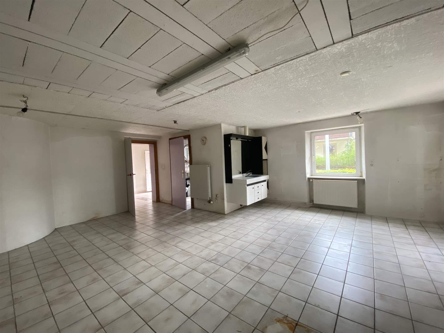 Großer leerer Raum mit Fliesenboden und Fenster