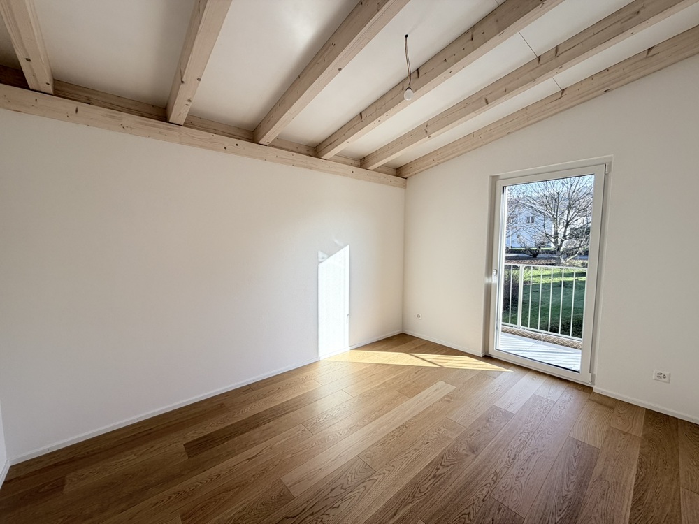 Leerer Wohnraum mit Holzbalkendecke und Balkonzugang