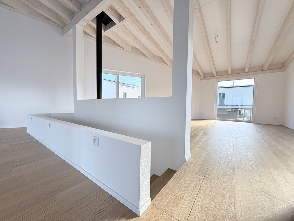 Heller, leerer Wohnraum mit sichtbaren Holzbalken und großer Fensterfront