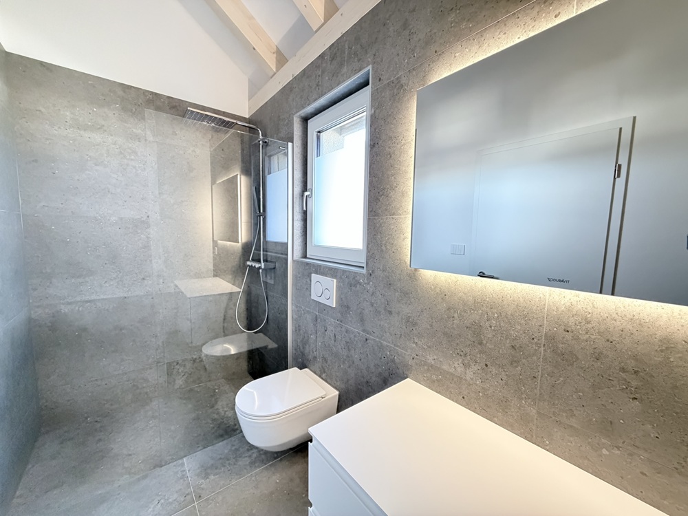 Modernes Badezimmer mit Dusche, WC und beleuchtetem Spiegel