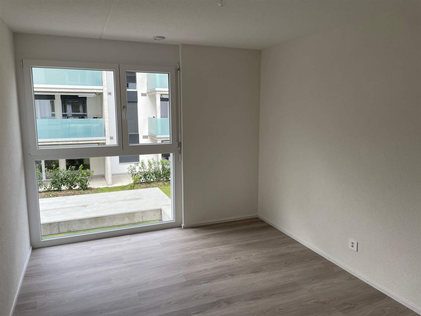 Helles, leeres Zimmer mit großem Fenster zur Wohnanlage