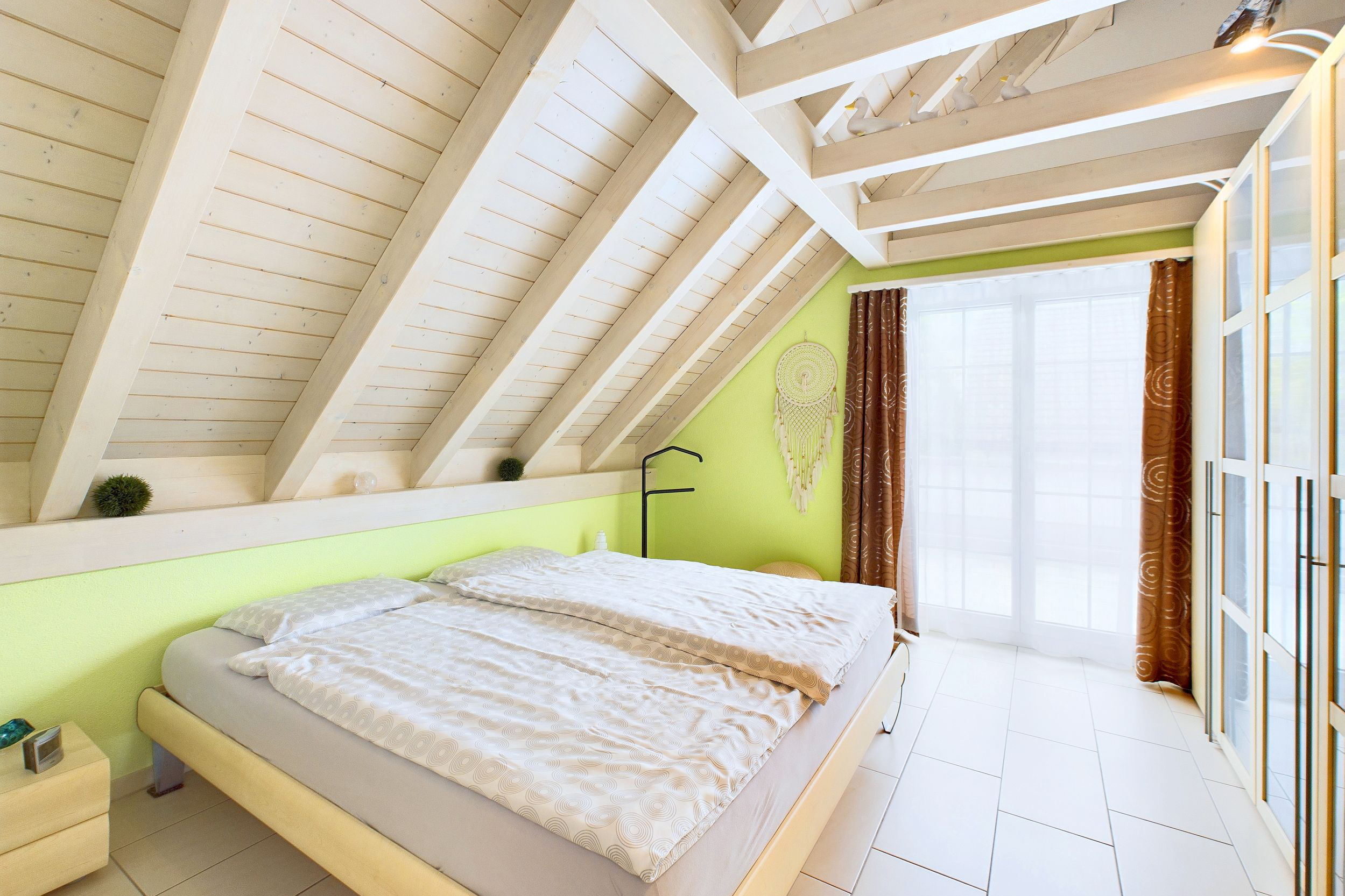 Helles Dachgeschoss-Schlafzimmer mit sichtbaren Holzbalken