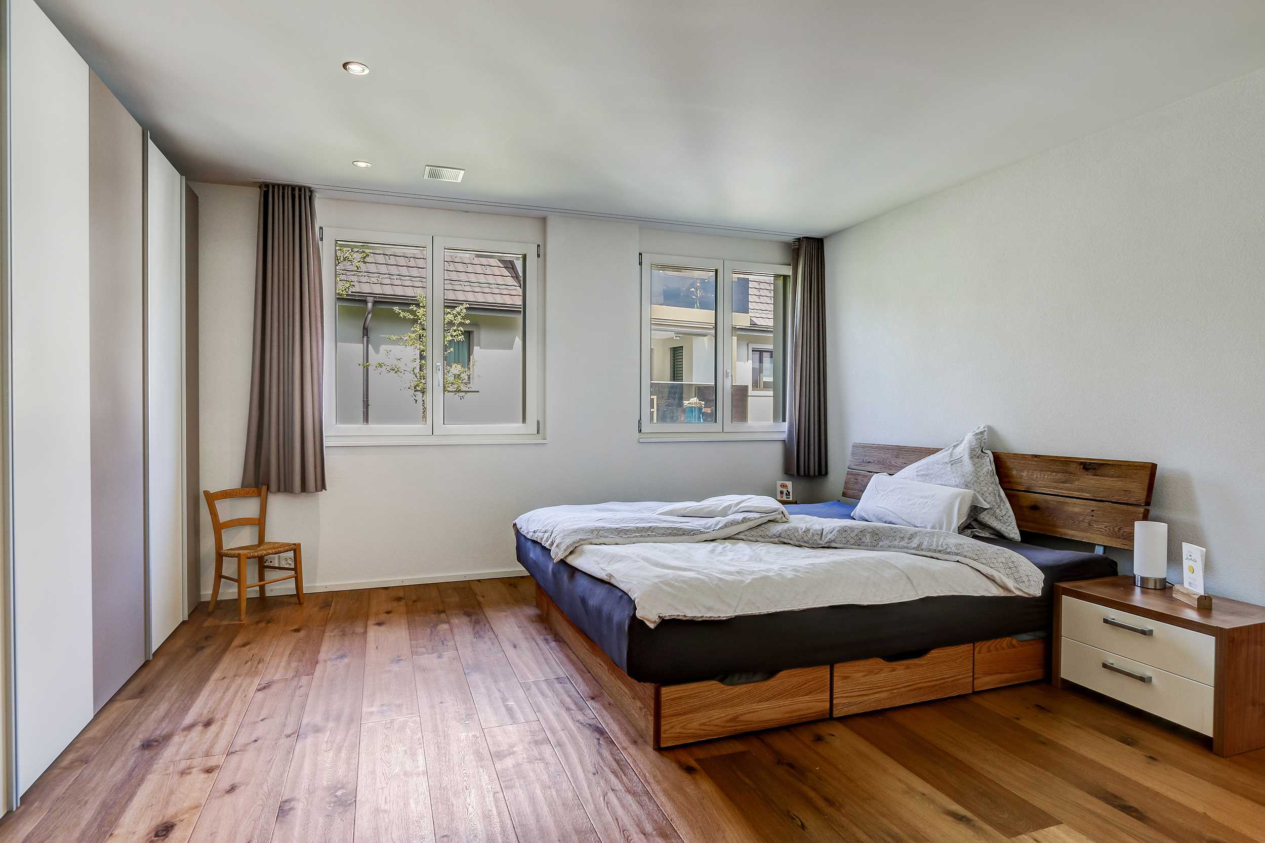 Schlafzimmer mit zwei Fenstern und Holzbett