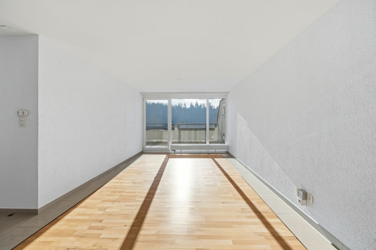 Heller leerer Wohnraum mit Balkon-/Terrassentür und Blick ins Grüne