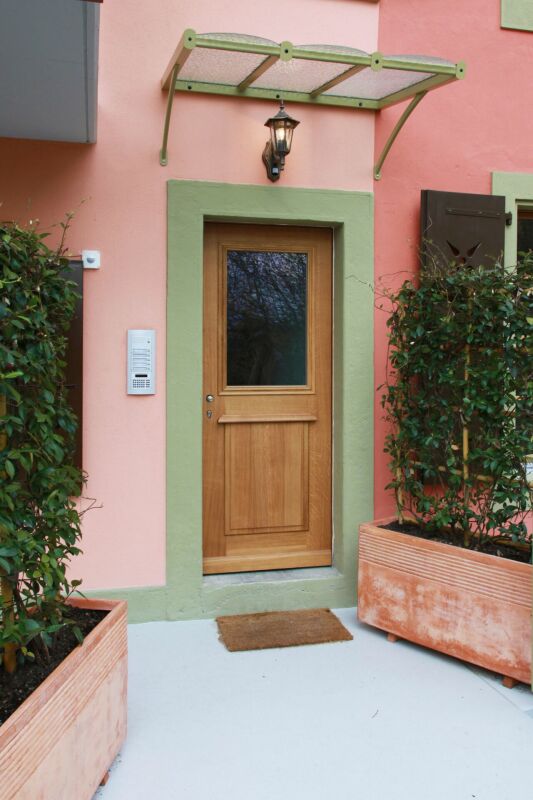 Eingangsbereich mit Holztür und rosa Fassade