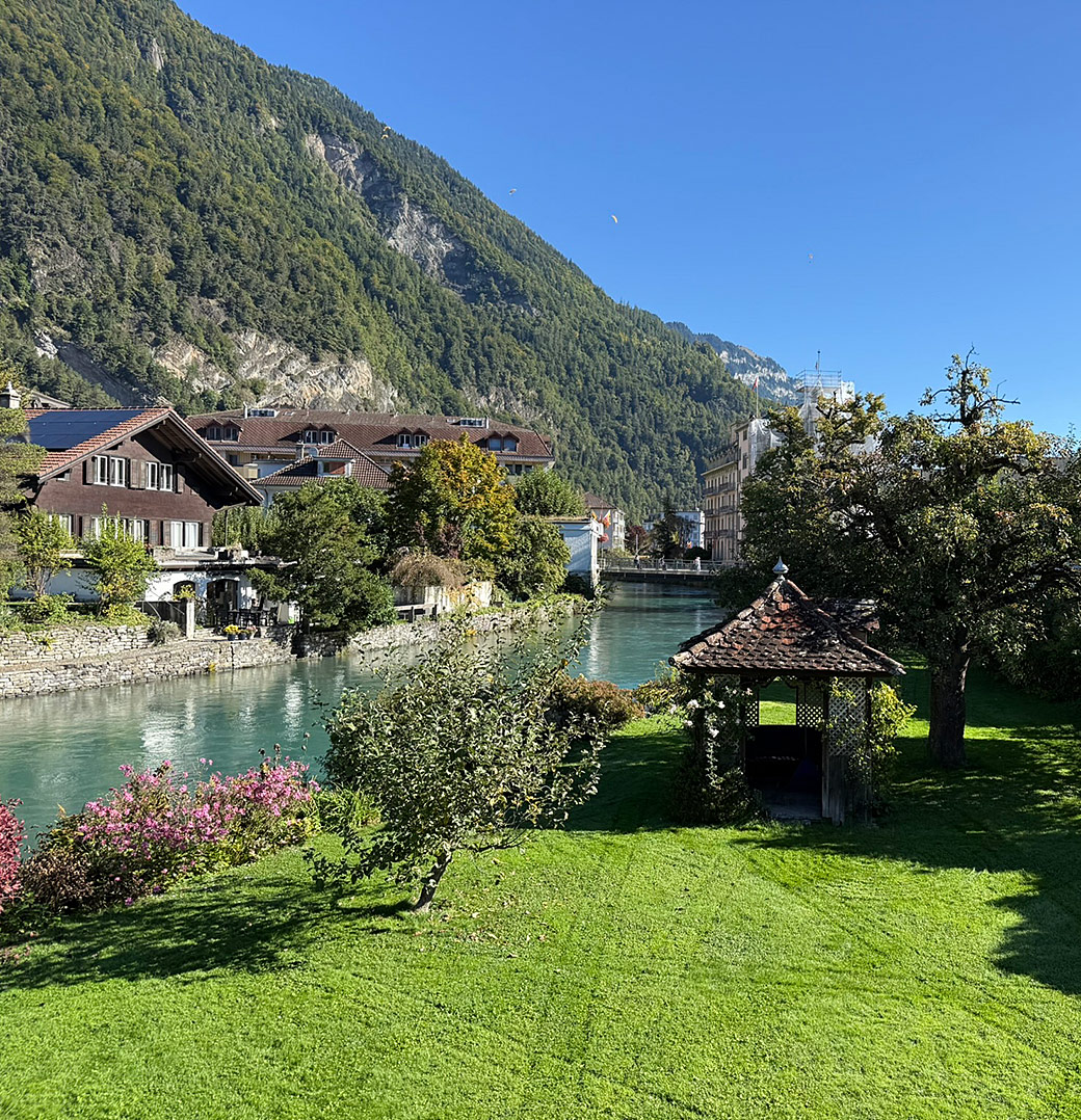 Flussufer mit Garten und Bergkulisse