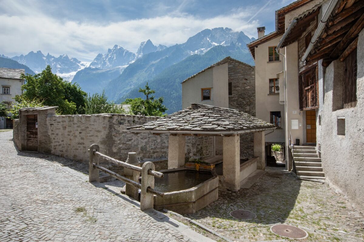 Historischer Dorfplatz mit Brunnen und Bergkulisse