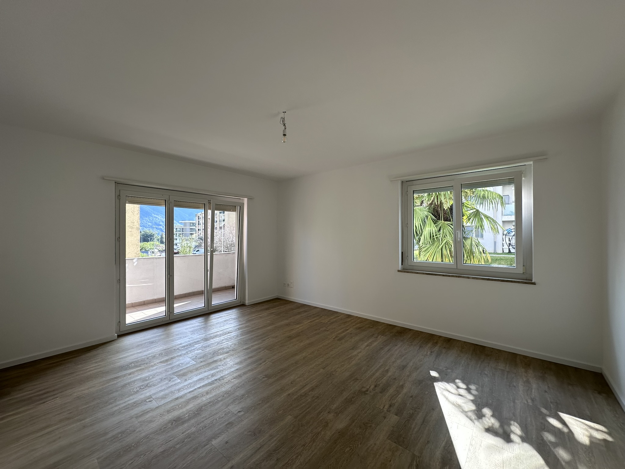 Heller leerer Wohnraum mit Balkon und zwei Fenstern
