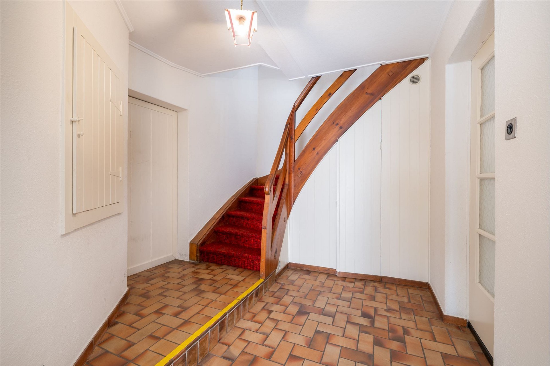 Treppenhaus mit Fliesenboden und roter Treppe