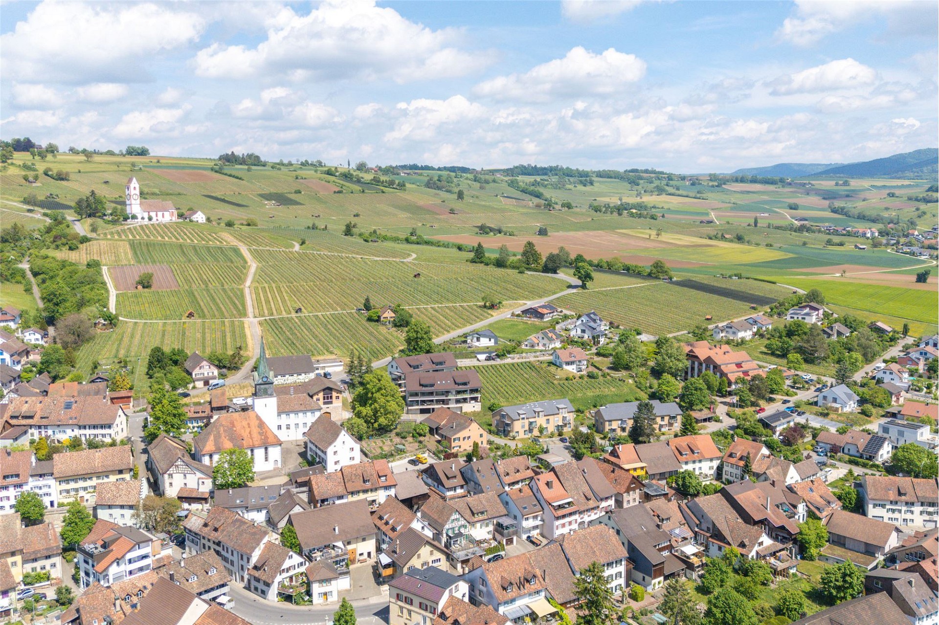 Luftaufnahme eines Dorfes in ländlicher Hügellandschaft