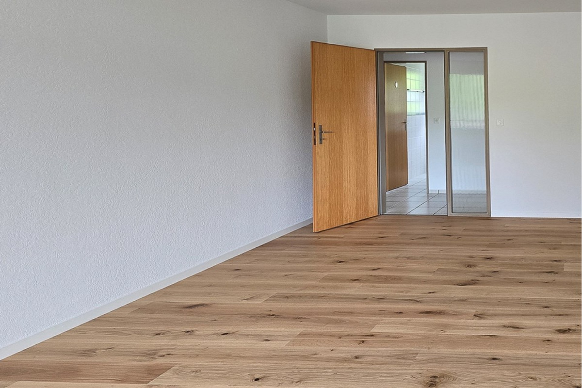 Leerer, renovierter Raum mit Holzoptikboden und offenstehender Tür