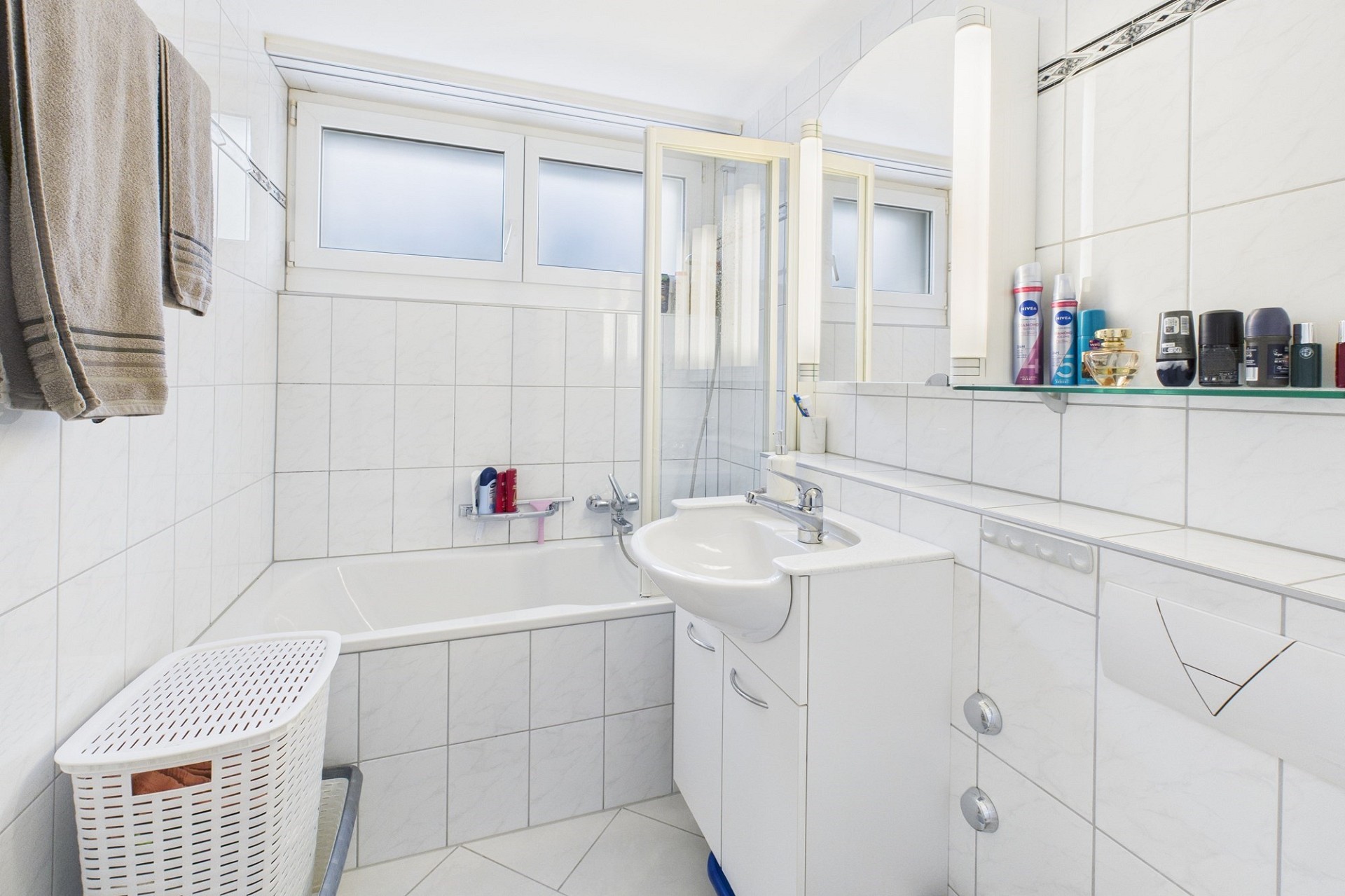 Kleines weiß gefliestes Badezimmer mit Badewanne und Waschtisch
