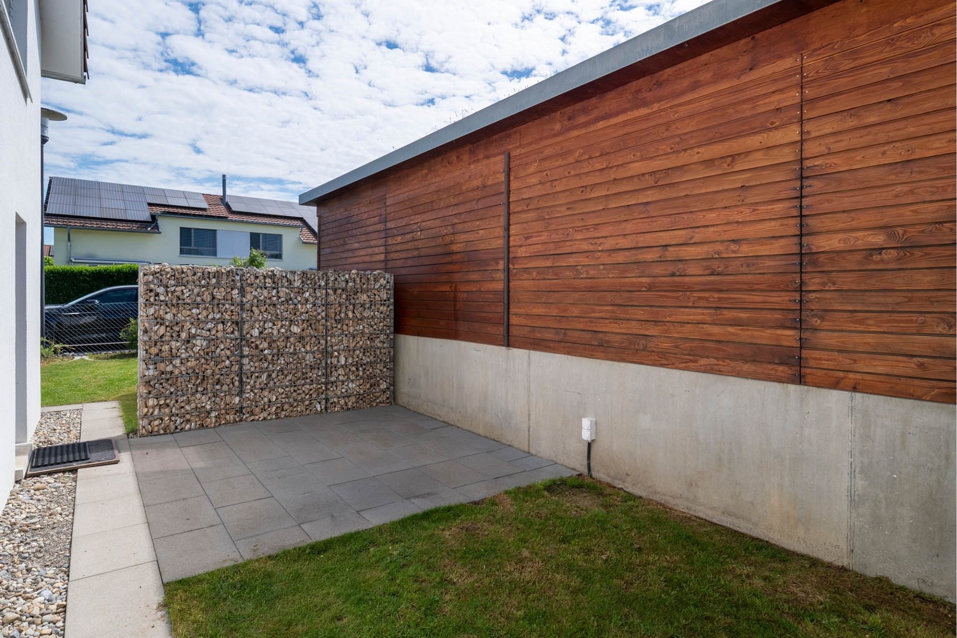 Moderner Außenbereich mit Holzfassade und Gabionenwand