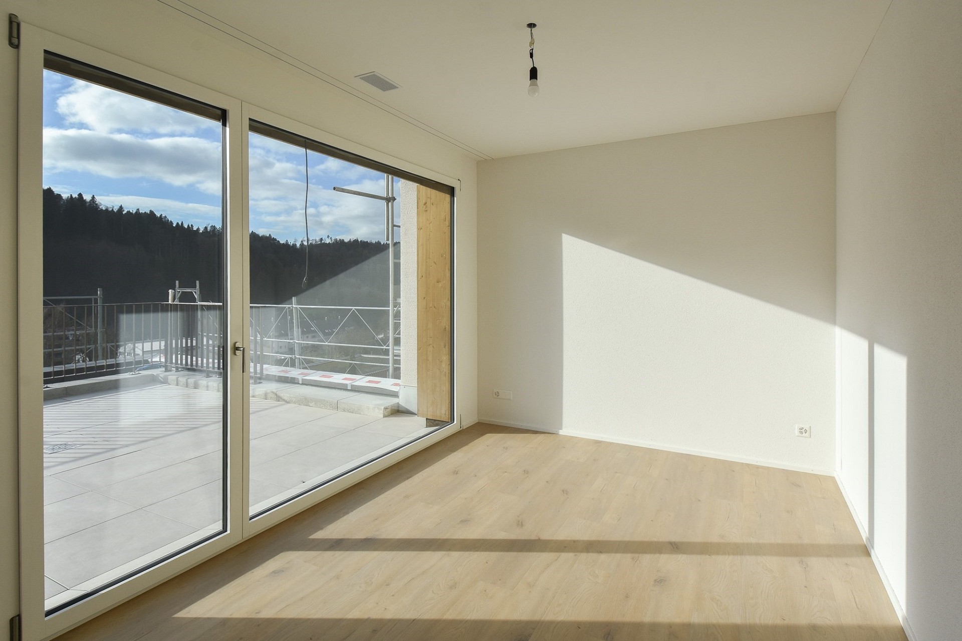 Helles, leeres Zimmer mit bodentiefer Verglasung und Balkonblick