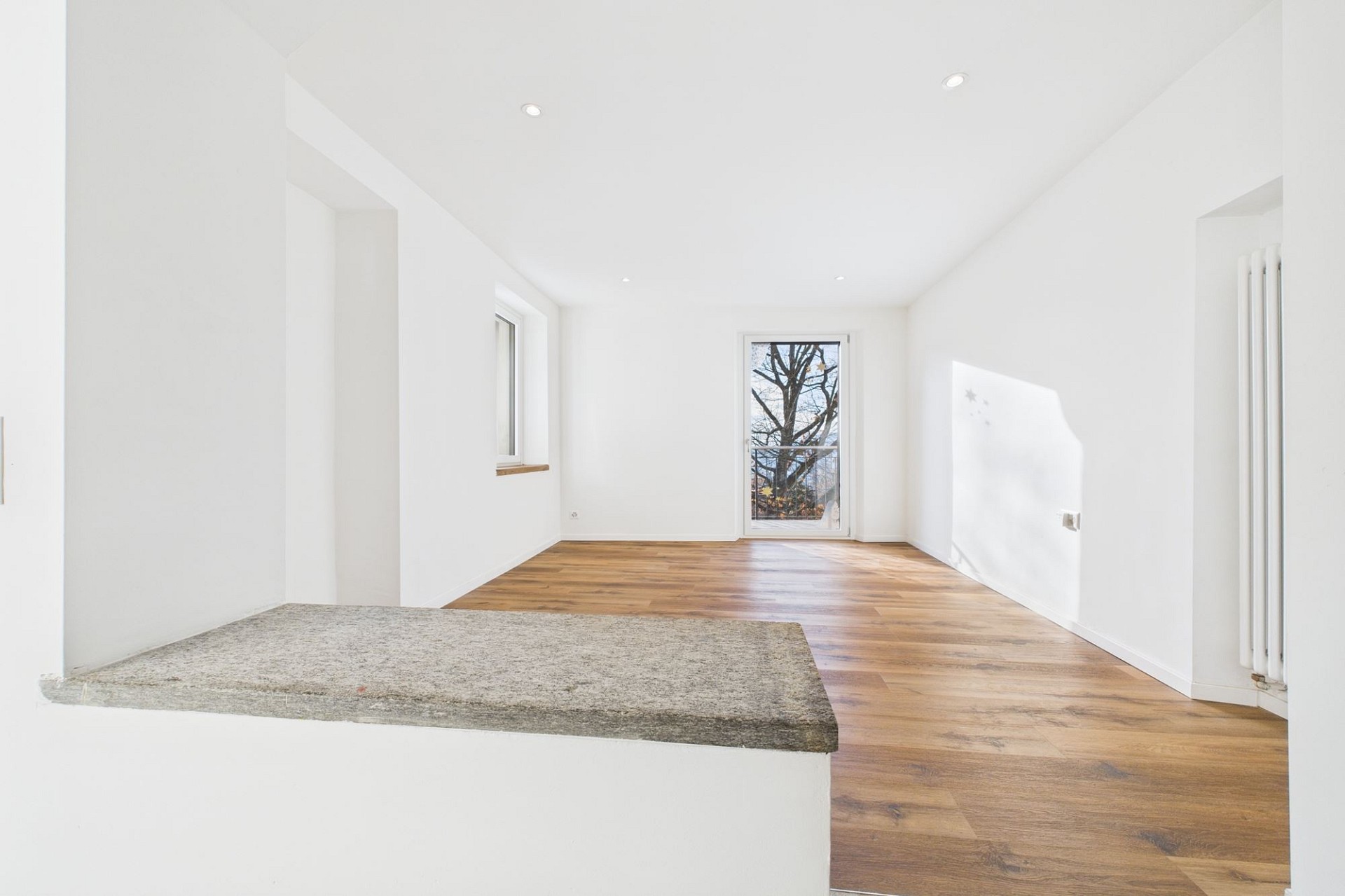 Heller leerer Innenraum mit Holzboden und Fenster/Tür zum Außenbereich