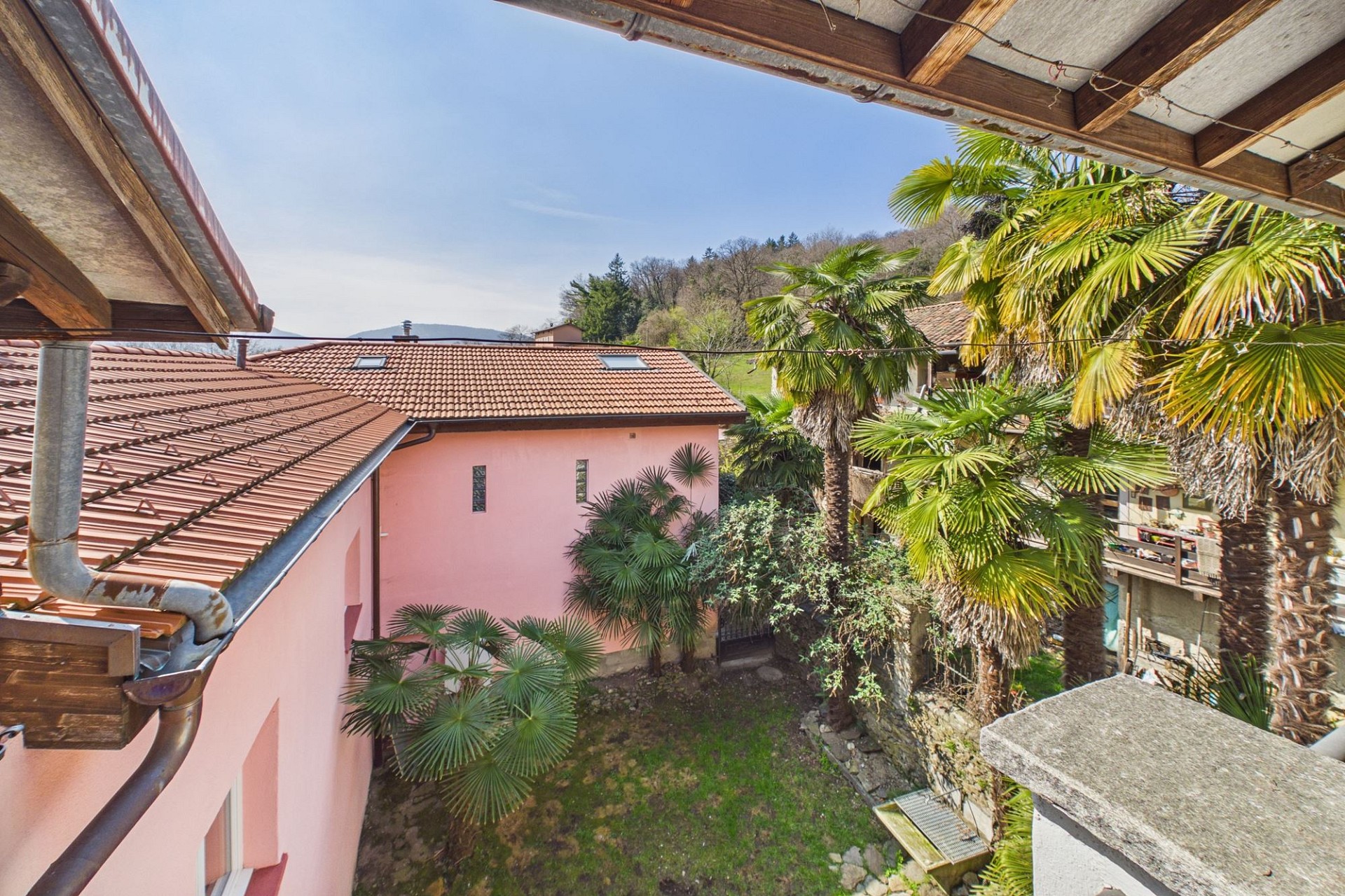Blick in einen begrünten Innenhof mit rosa Fassade und Ziegeldach
