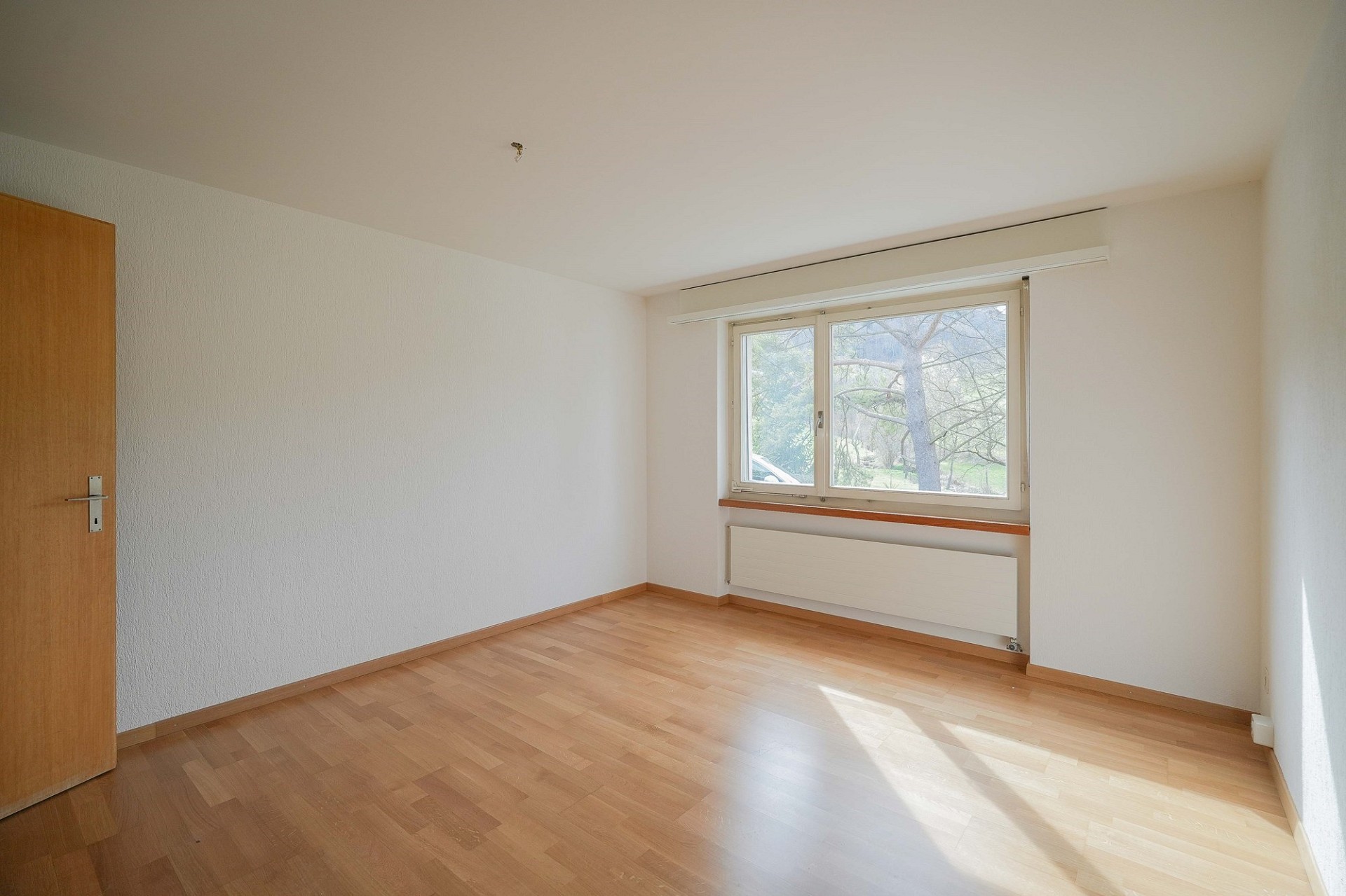 Helles, leeres Zimmer mit Fenster und Holzboden