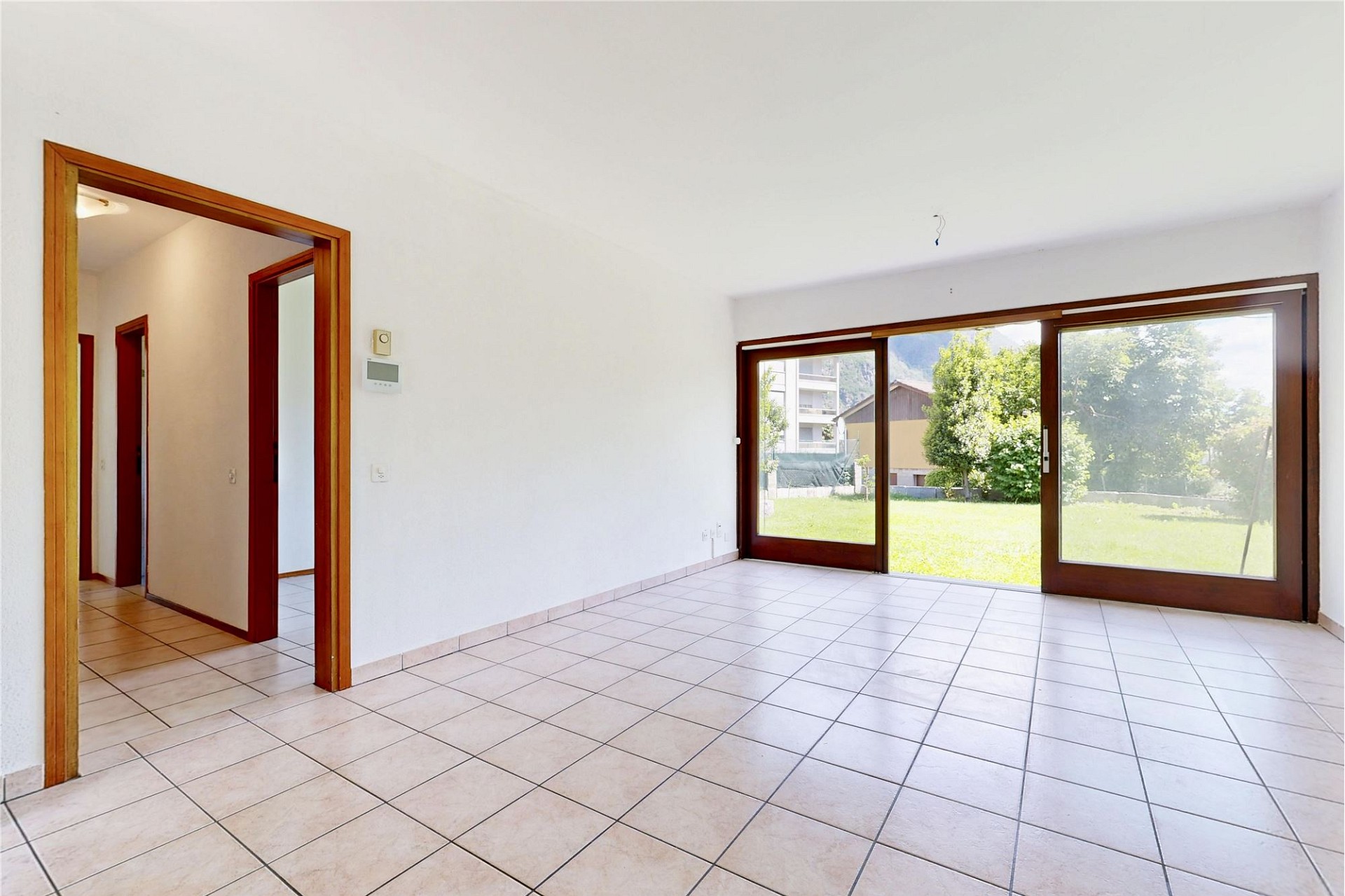 Heller leerer Wohnraum mit großem Schiebetürfenster zum Garten