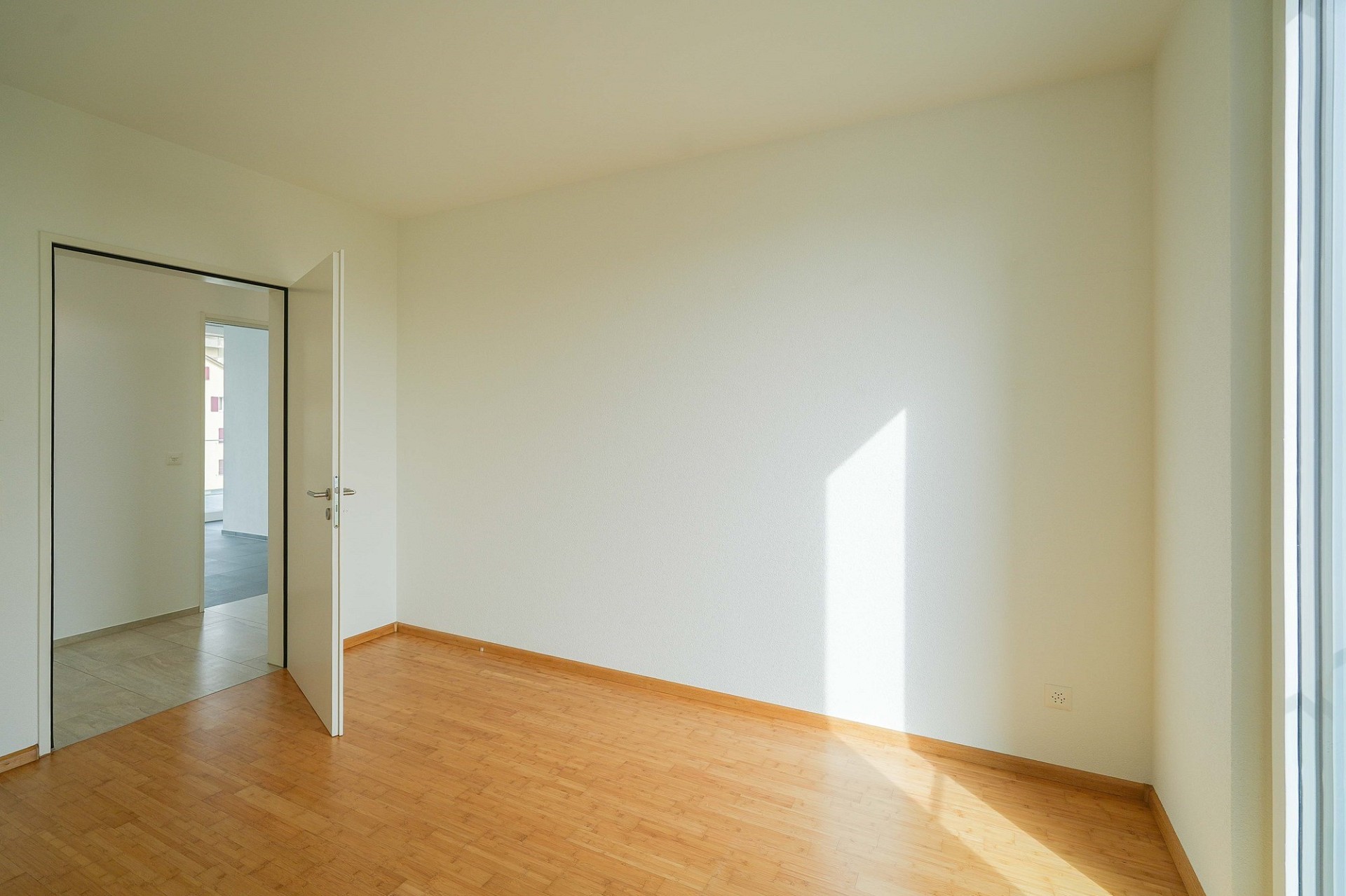 Helles, leeres Zimmer mit Holzoptik-Boden