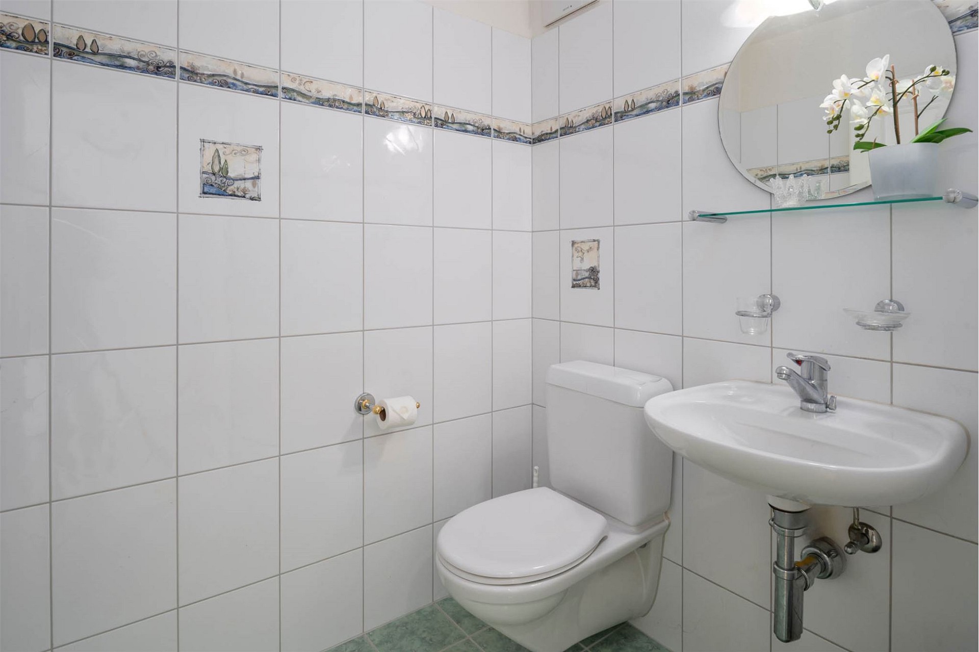Kleines Gäste-WC mit weißen Fliesen und dekorativer Bordüre