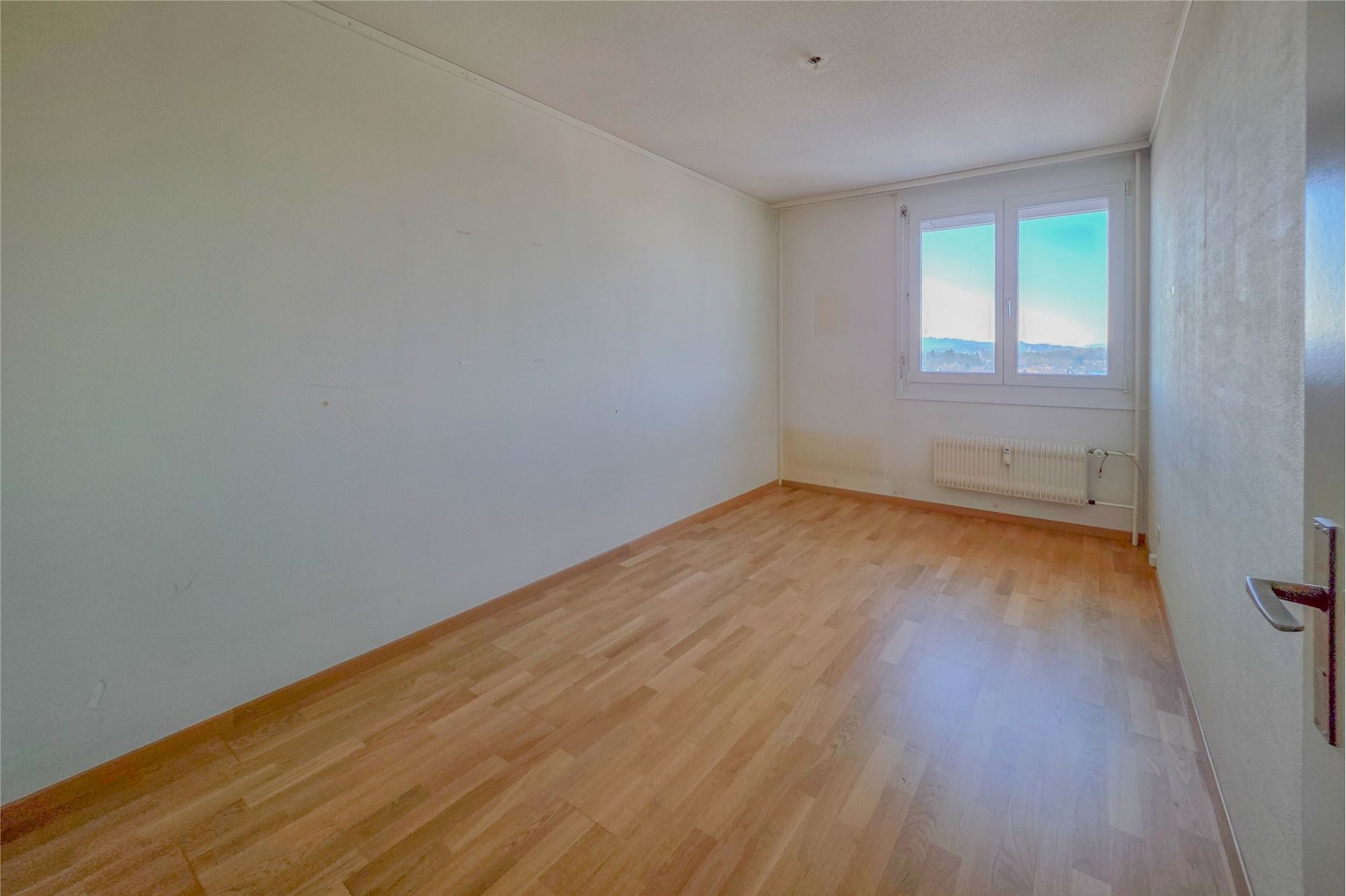 Leeres Zimmer mit Holzoptik-Boden und Fensterblick