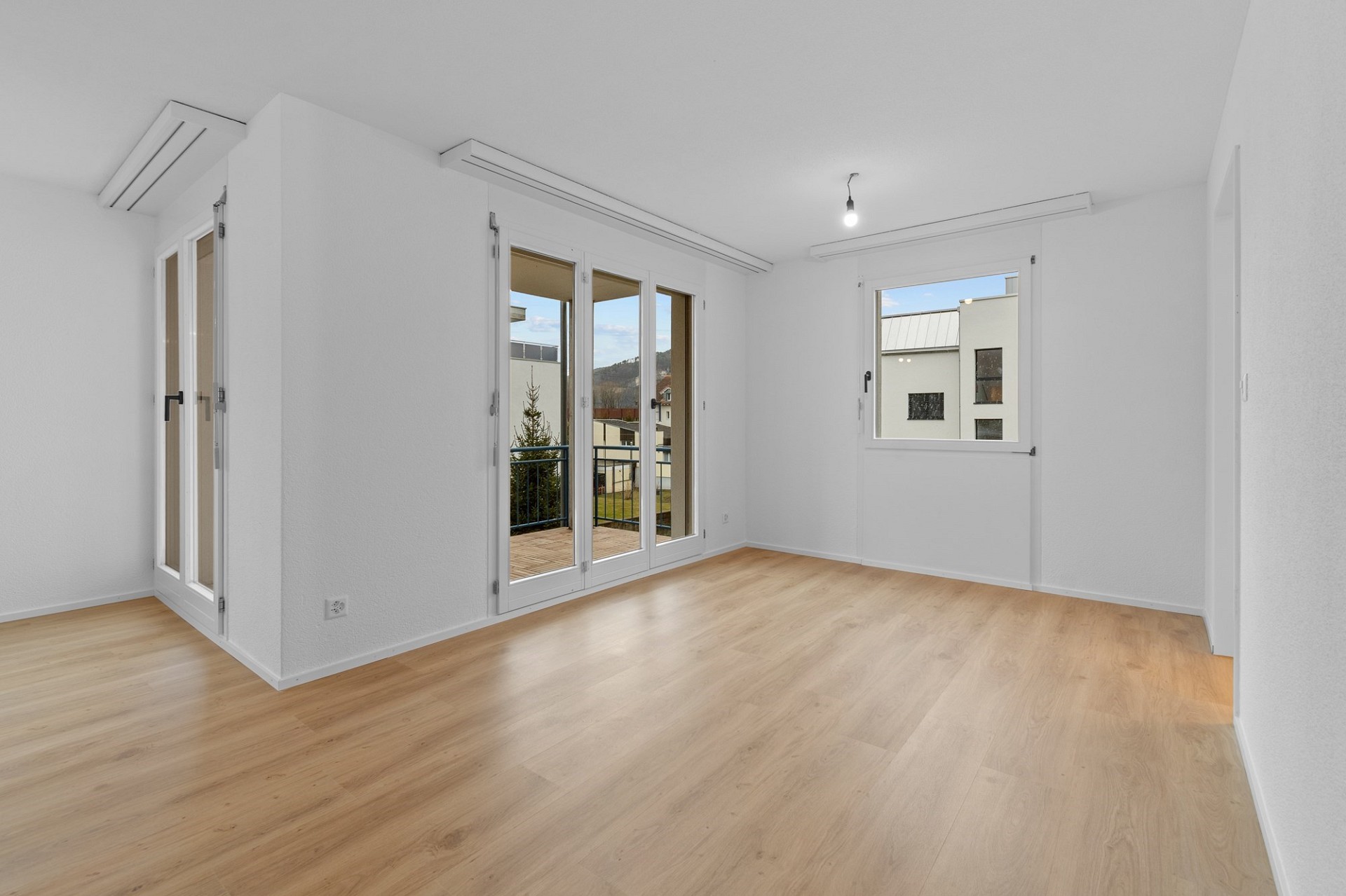 Helles, leeres Zimmer mit Holzboden und vielen Fenstern