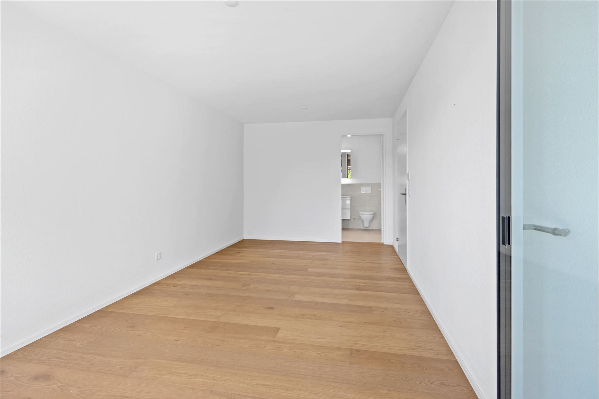 Heller leerer Innenraum mit Holzboden und angeschlossenem Bad