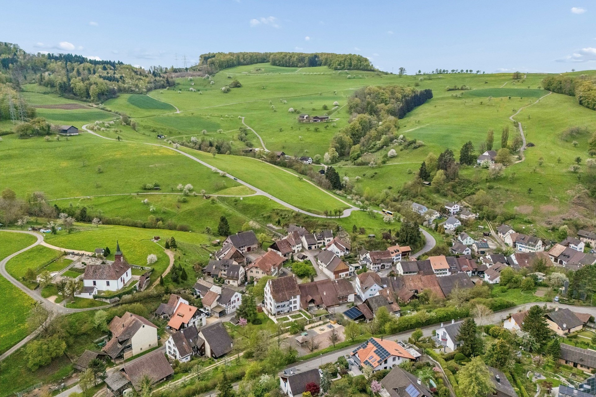 Luftaufnahme eines ländlichen Dorfes in grüner Hügellandschaft