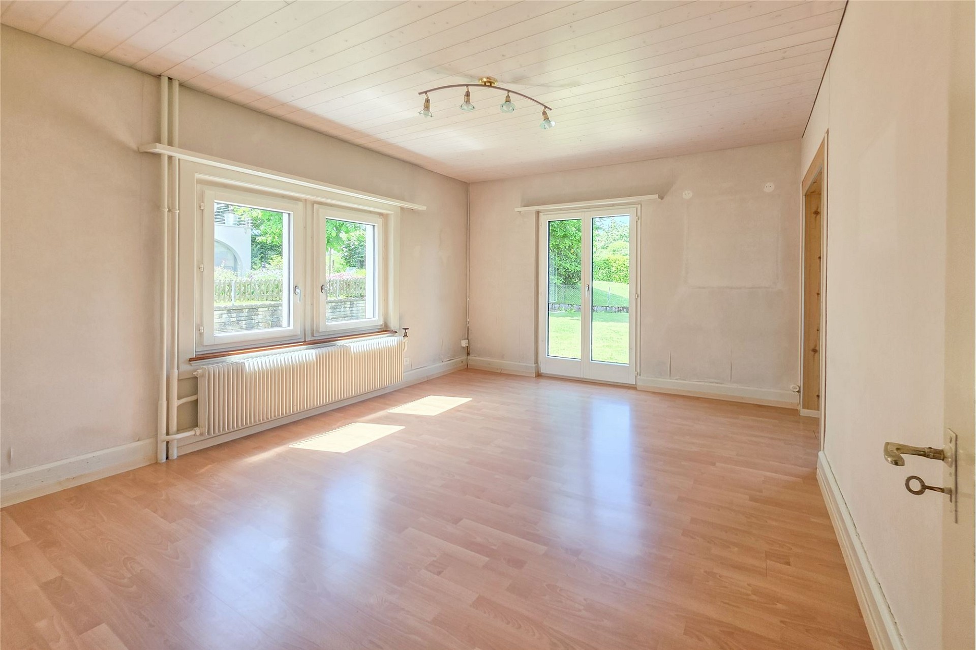 Heller leerer Raum mit Fensterfront und Gartenzugang
