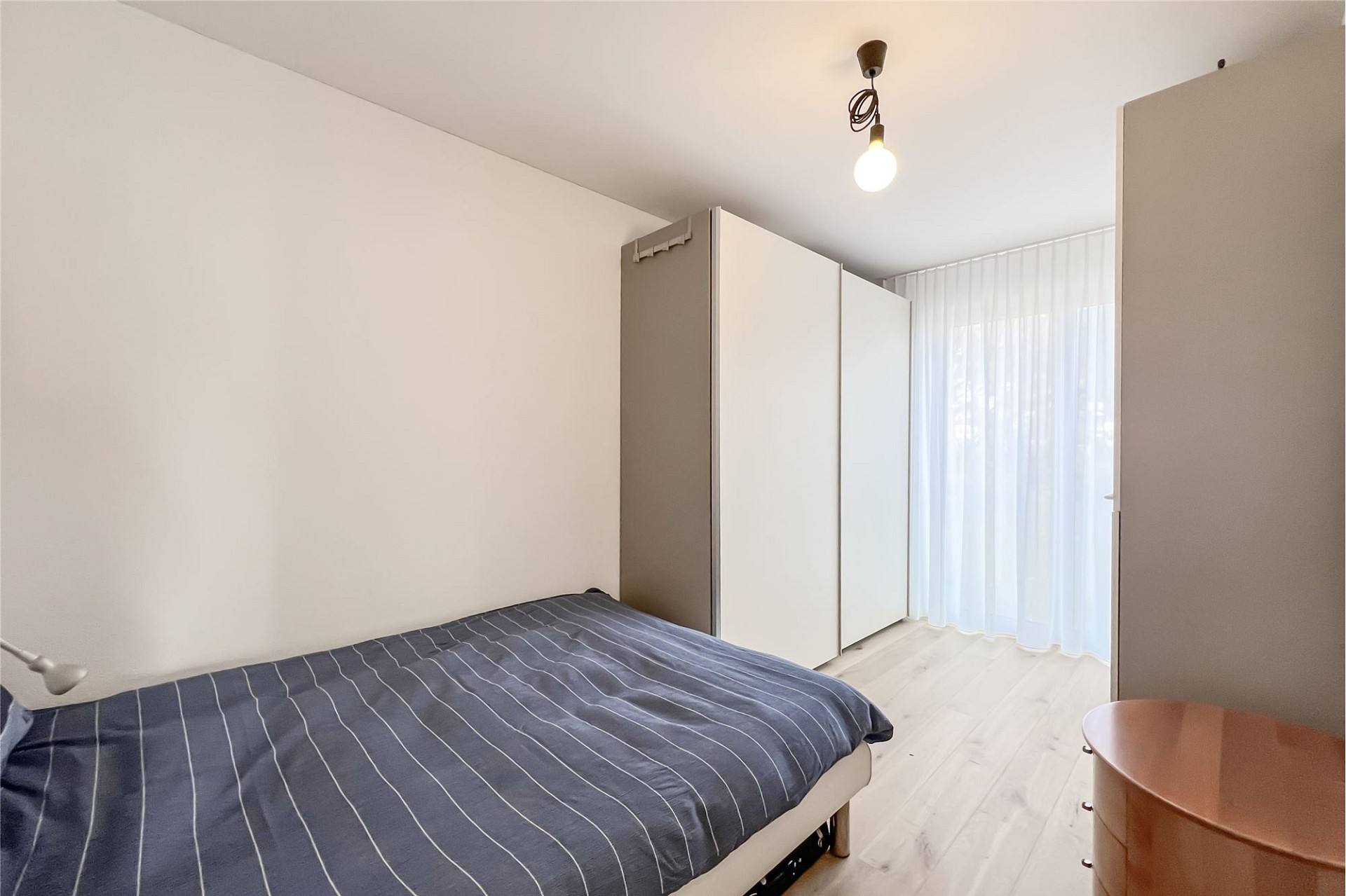 Kleines Schlafzimmer mit schlichtem Doppelbett und Schrankwand
