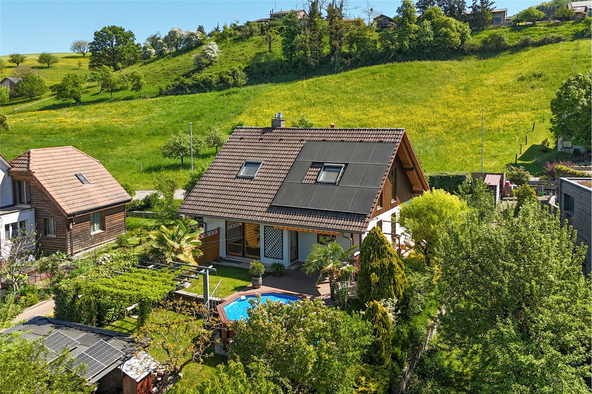 Luftaufnahme eines Hauses mit Garten und Pool in grüner Hanglage