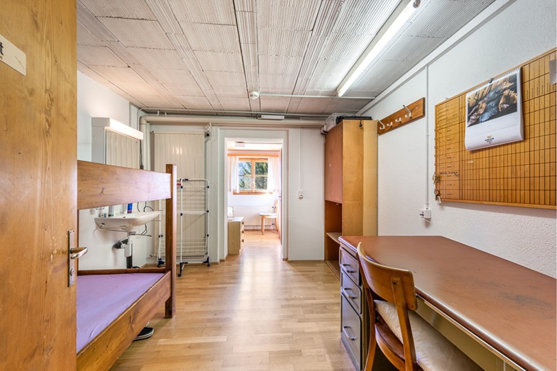 Einfaches Zimmer mit Bett, Schreibtisch und Waschbecken