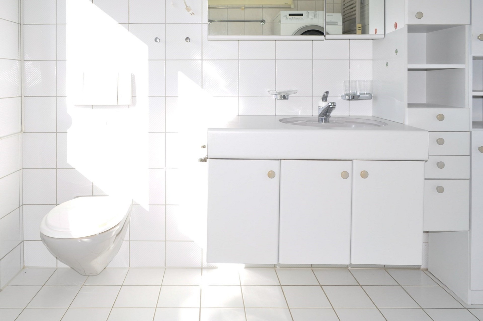 Kleines, weiß gefliestes Badezimmer mit WC und Waschtisch