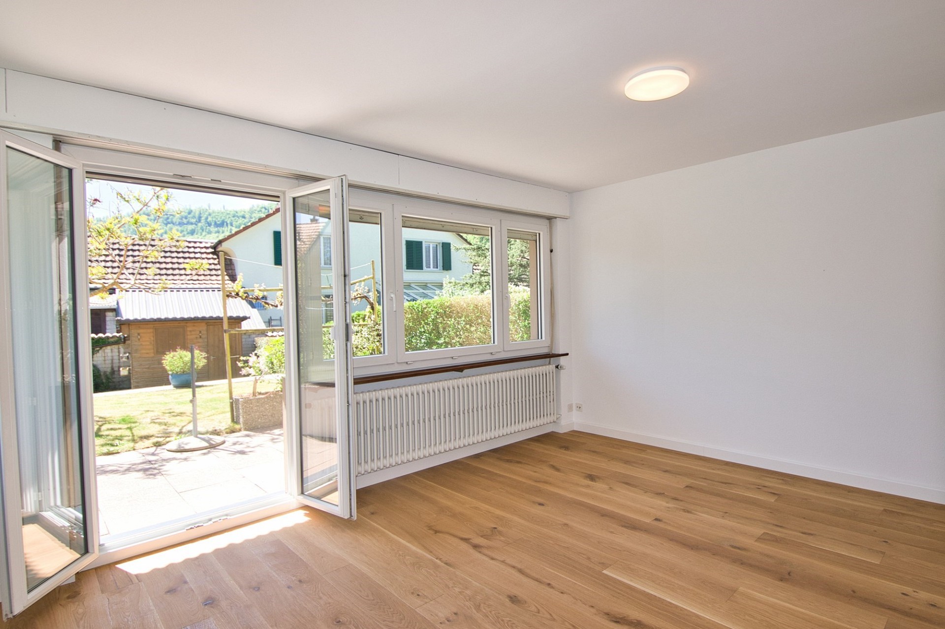 Heller leerer Wohnraum mit Terrassentür und Gartenblick