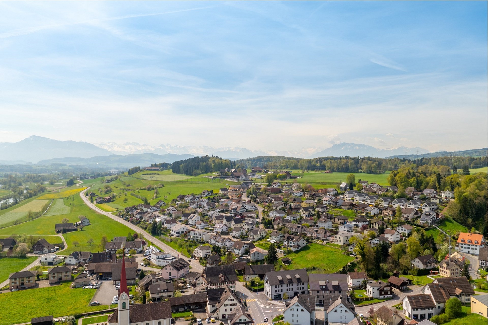 Luftaufnahme eines Dorfes in einer grünen Alpenlandschaft