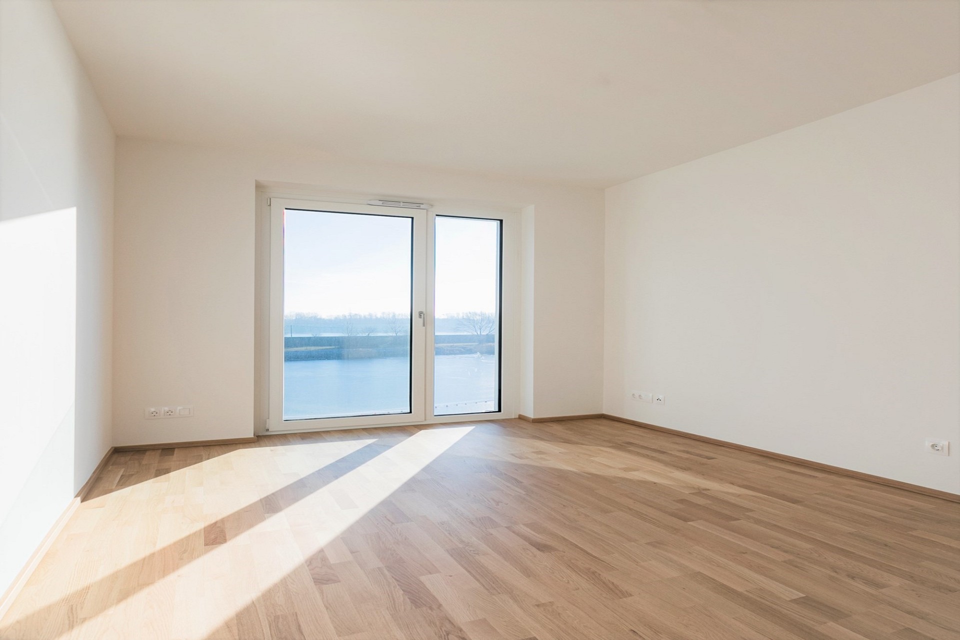 Heller leerer Wohnraum mit großem Fenster und Holzboden