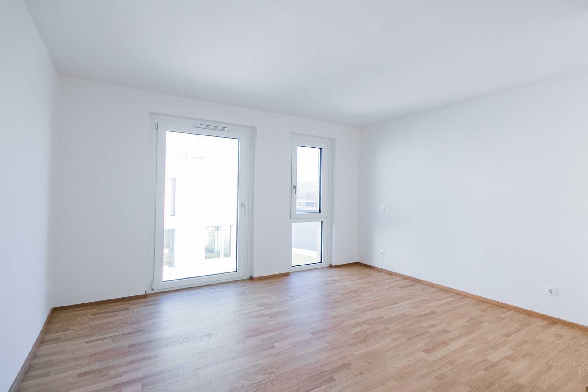 Helles, leeres Zimmer mit Balkon- bzw. Fenstertüren